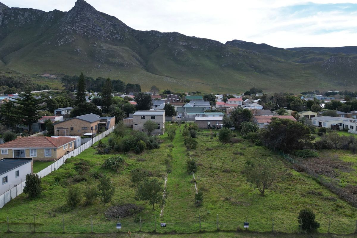 An aerial view of a vacant residential plot featuring established vegetation and perimeter fencing, set against a scenic mountain backdrop.