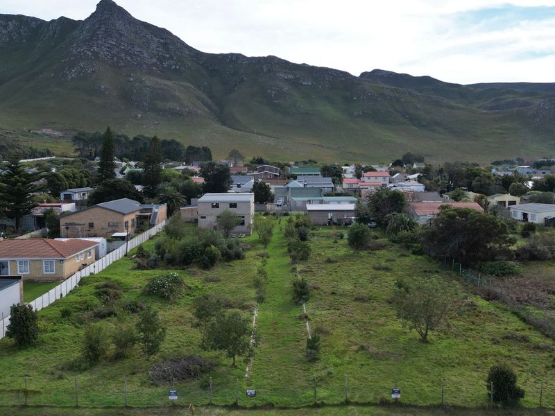 An aerial view of a vacant residential plot featuring established vegetation and perimeter fencing, set against a scenic mountain backdrop.