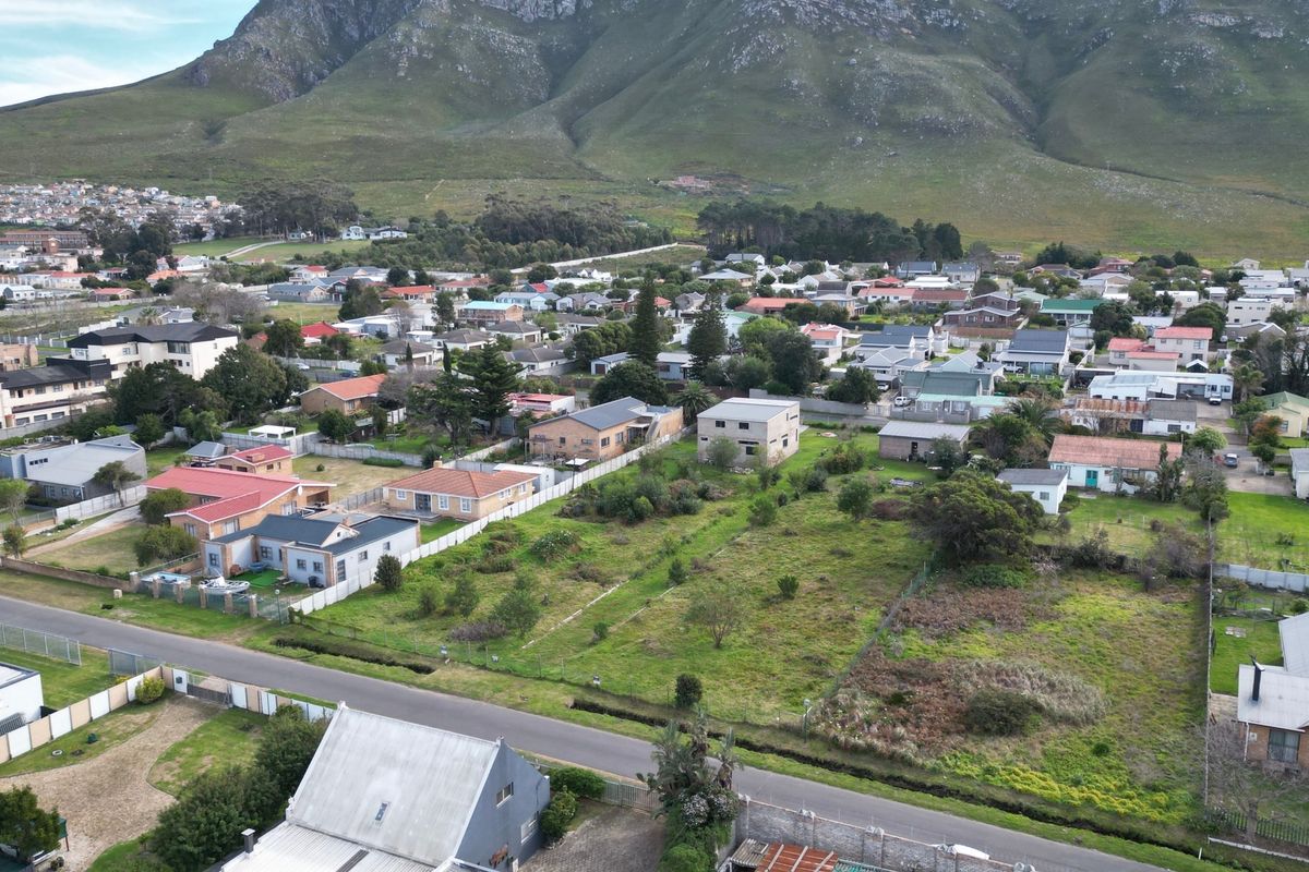 An aerial view of a vacant residential plot situated in a developed neighborhood with scenic mountain views in the background.