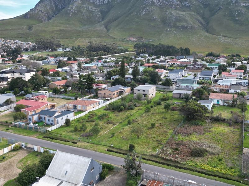 An aerial view of a vacant residential plot situated in a developed neighborhood with scenic mountain views in the background.