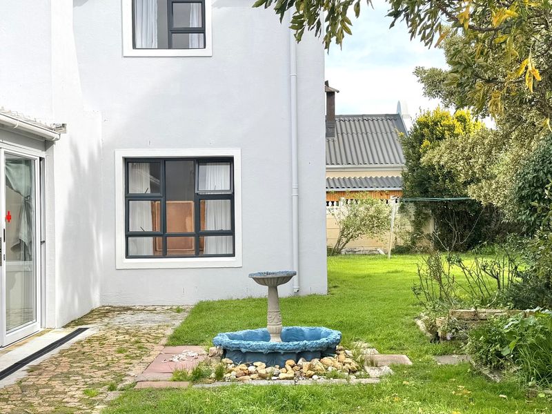 Rear view of the property featuring a paved patio area, sliding glass doors, and a private garden with lawn.