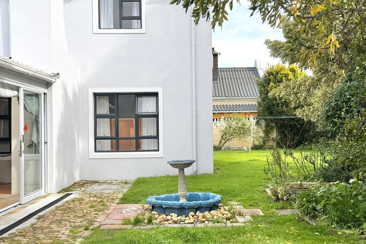 Rear view of the property featuring a paved patio area, sliding glass doors, and a private garden with lawn.