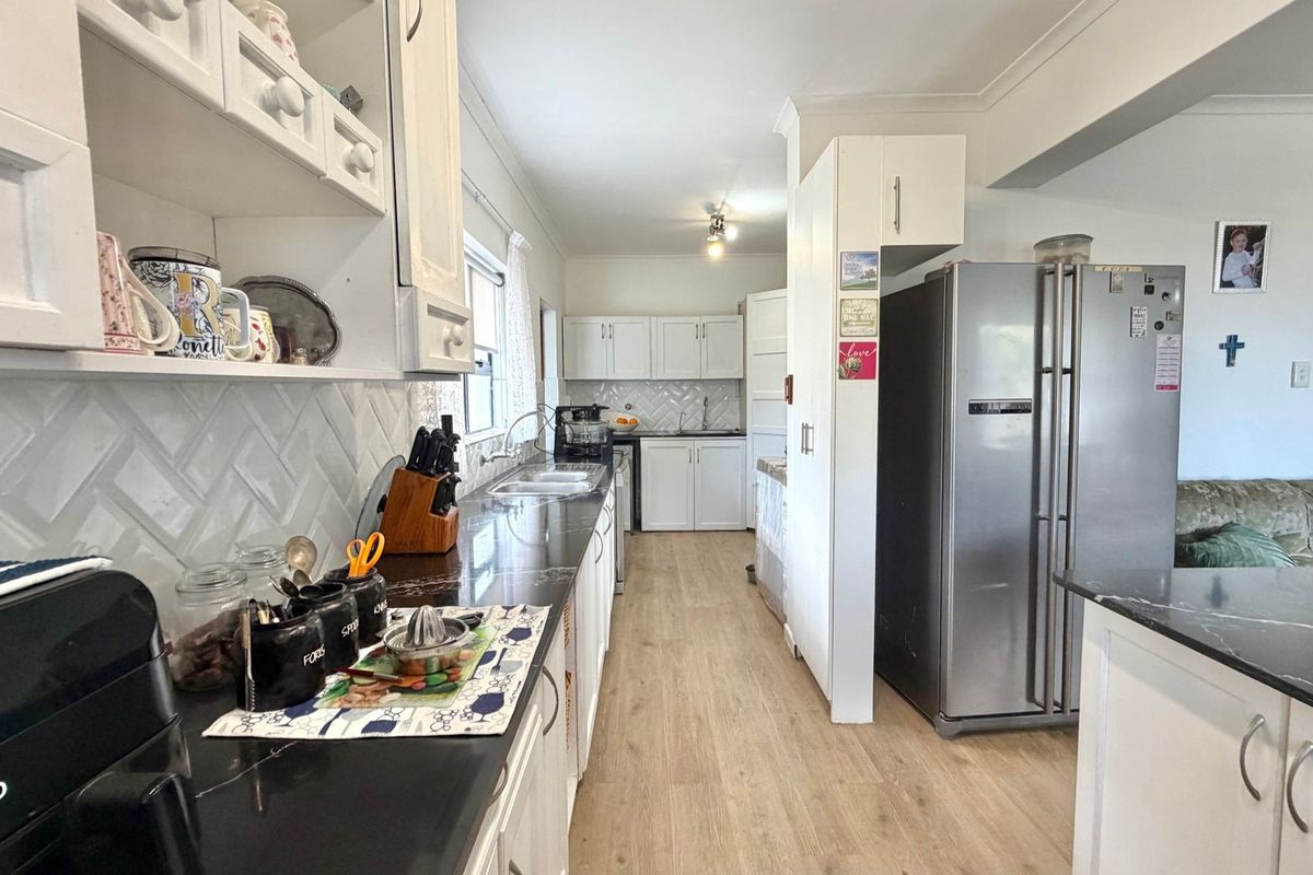 A functional kitchen featuring white cabinetry, dark countertops, a herringbone tile backsplash, and light-toned laminate flooring.