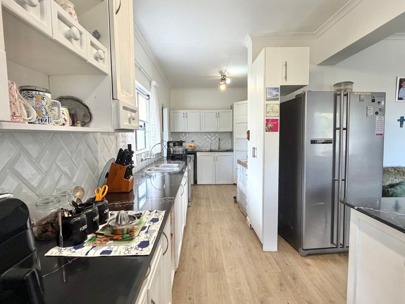A functional kitchen featuring white cabinetry, dark countertops, a herringbone tile backsplash, and light-toned laminate flooring.