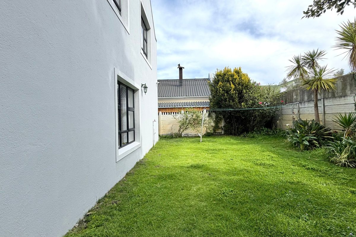 A side view of the property showing a well-maintained lawn, plastered exterior walls, and secure boundary fencing.