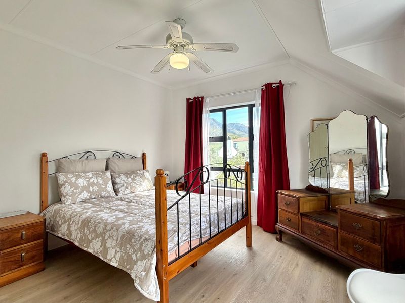 A well-lit bedroom featuring laminate flooring, a ceiling fan, and a sloped ceiling with a window offering mountain views.