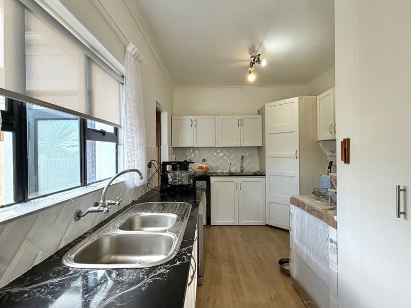 Functional scullery featuring double bowl sink, laminate countertops, herringbone tile backsplash, and ample built-in cabinetry for additional storage and prep space.