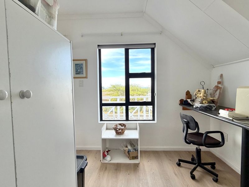 A bedroom or home office space featuring laminate flooring, a sloped ceiling, and a built-in desk area with natural light from the window.