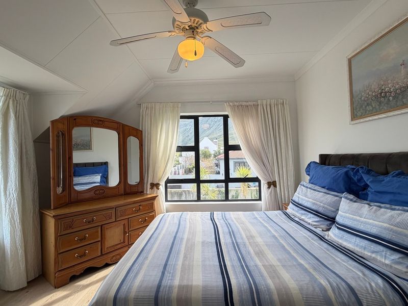 A well-lit bedroom featuring a ceiling fan, coved ceilings, and large windows providing natural light and exterior views.