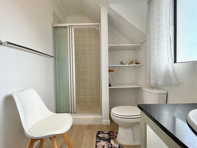 A functional bathroom featuring a shower enclosure, toilet, vanity basin, and convenient built-in shelving under the eaves.