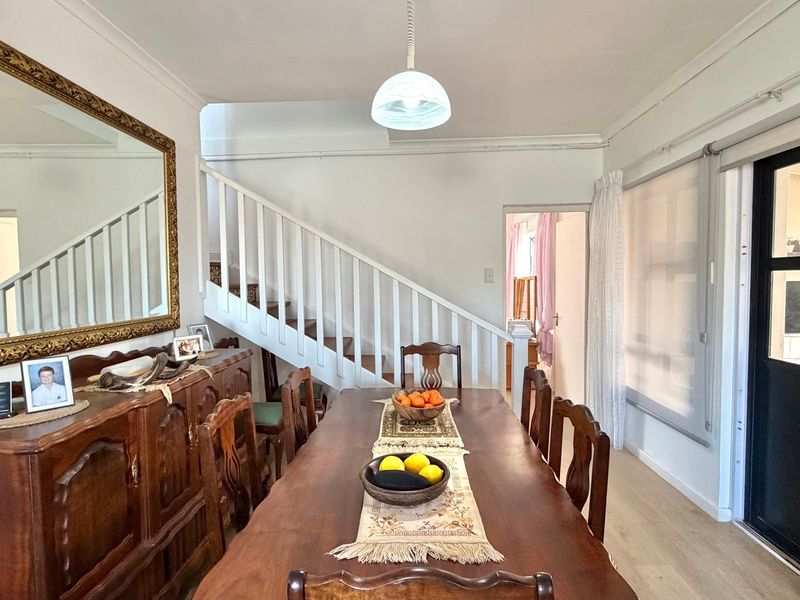 A dining room featuring a staircase with a white balustrade, pendant lighting, and a sliding door leading to an adjacent space.