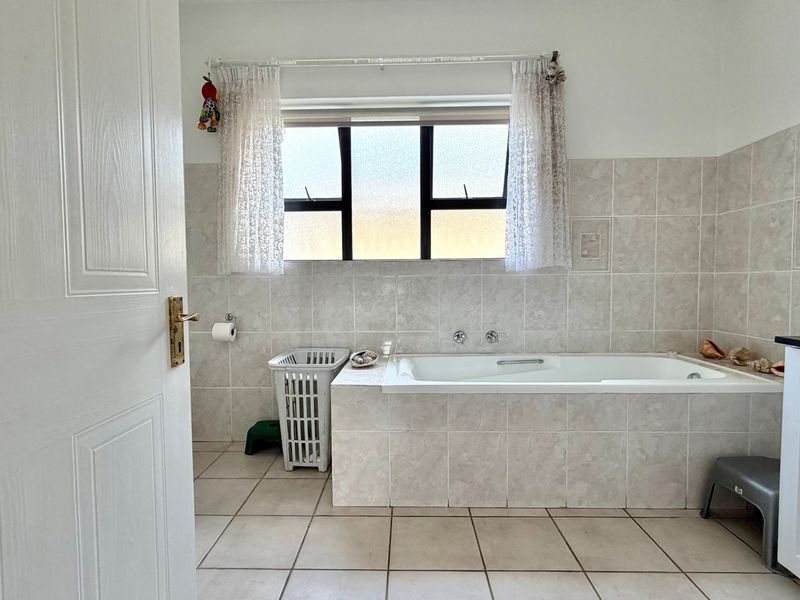A functional bathroom featuring a built-in bathtub, tiled walls and flooring, and a vanity cabinet with a dark countertop.