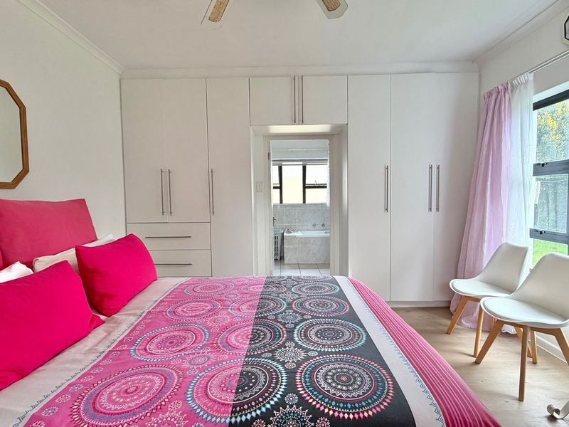 Spacious bedroom featuring extensive built-in cupboards, laminate flooring, and an en-suite bathroom access point with large windows allowing natural light.