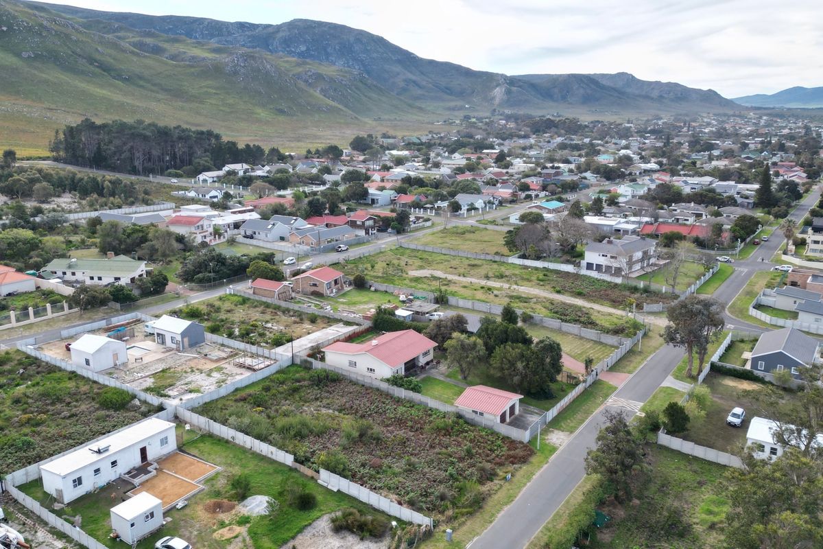 Aerial view of a residential neighborhood featuring vacant land plots, established homes, and paved streets set against a scenic mountain landscape.