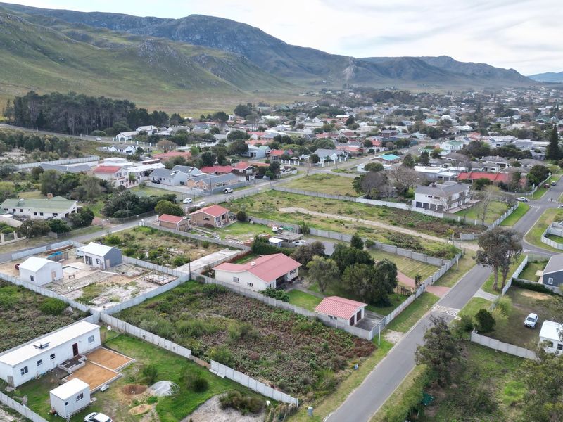 Aerial view of a residential neighborhood featuring vacant land plots, established homes, and paved streets set against a scenic mountain landscape.