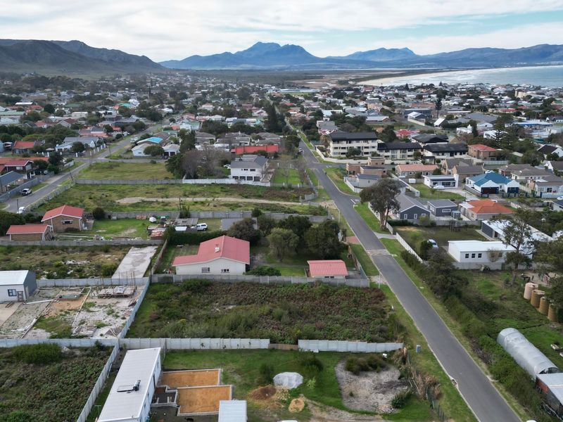 Aerial view of a residential neighborhood featuring vacant land plots, established homes, and proximity to the coastline and mountain range.