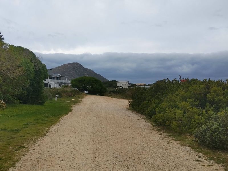 A view of a gravel access road leading through a natural landscape with surrounding vegetation and distant mountain views.
