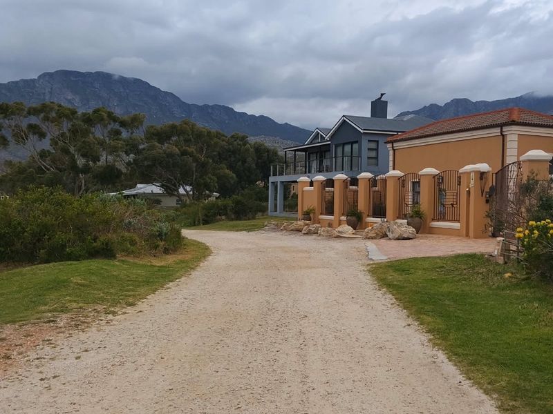A gravel driveway leading to a residential property with a perimeter wall, wrought iron fencing, and scenic mountain views.