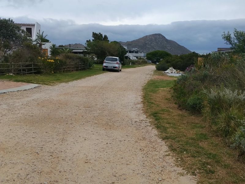 A view of a gravel access road leading through a residential area with surrounding natural vegetation and mountain views in the distance.