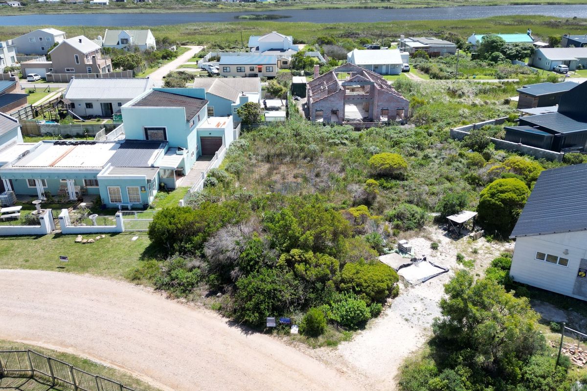 An aerial view of a vacant residential plot situated in a coastal neighborhood, surrounded by established homes and natural vegetation.