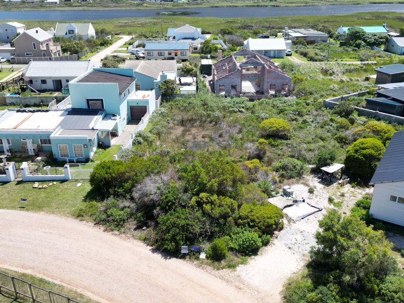 An aerial view of a vacant residential plot situated in a coastal neighborhood, surrounded by established homes and natural vegetation.