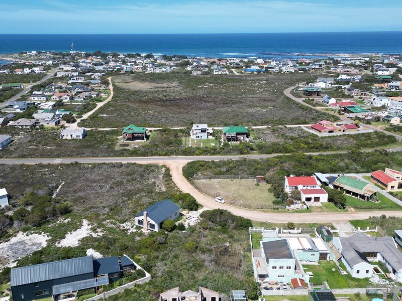 An aerial view of a coastal residential area featuring vacant land plots, established homes, and proximity to the ocean.