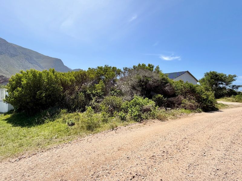 A view of the gravel road frontage and perimeter fencing bordering the vacant residential land, set against a mountain backdrop.