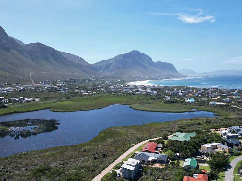 An expansive aerial view showcasing the coastal residential area, surrounding wetlands, and scenic mountain backdrop.