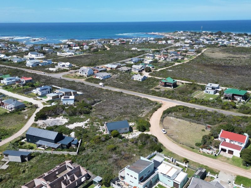 An aerial view of a coastal residential area featuring vacant land plots, established homes, and proximity to the ocean.