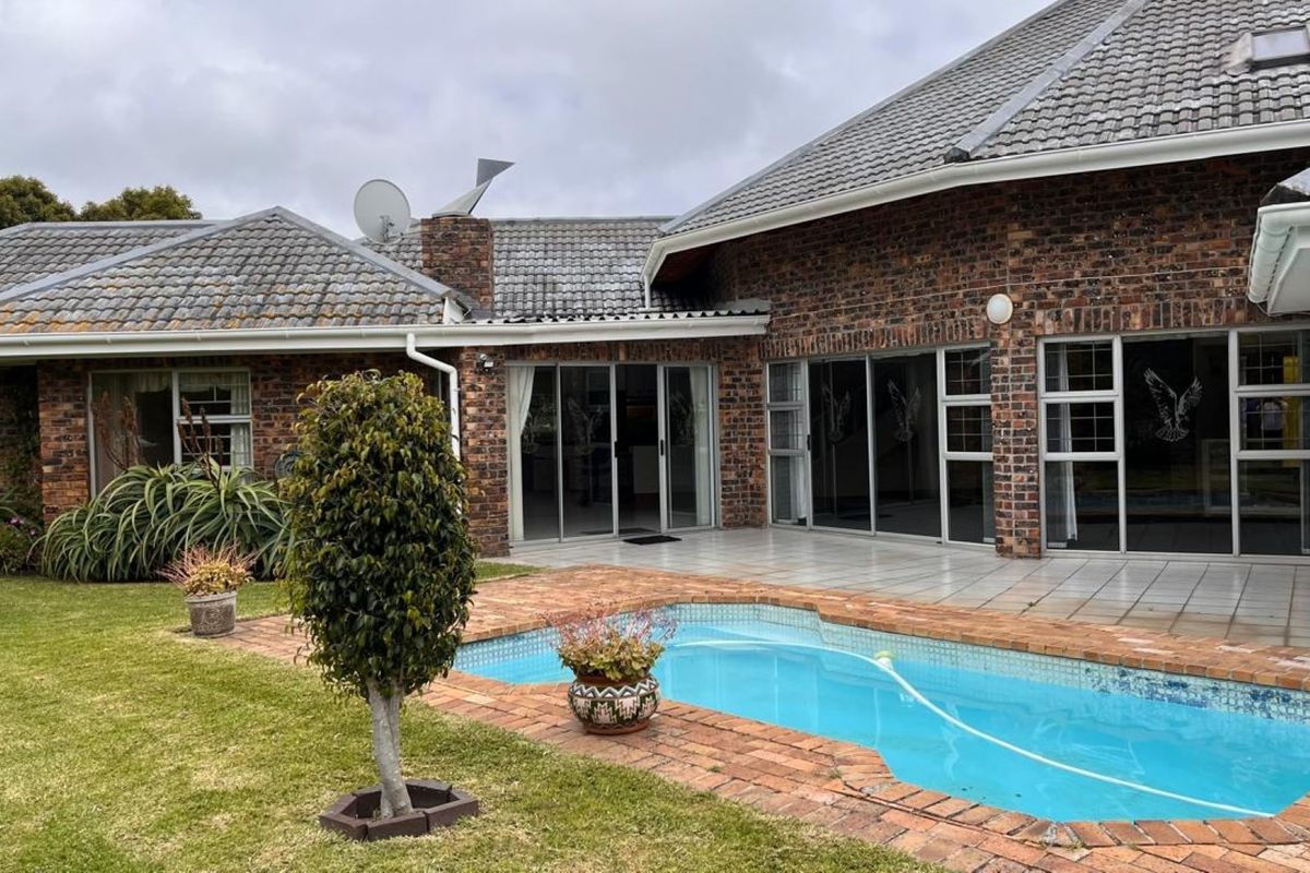 Rear view of a face brick house featuring a swimming pool, paved surround, and multiple sliding glass doors leading to the interior.