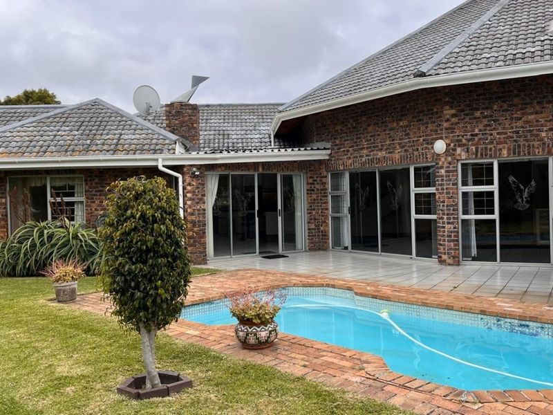 Rear view of a face brick house featuring a swimming pool, paved surround, and multiple sliding glass doors leading to the interior.