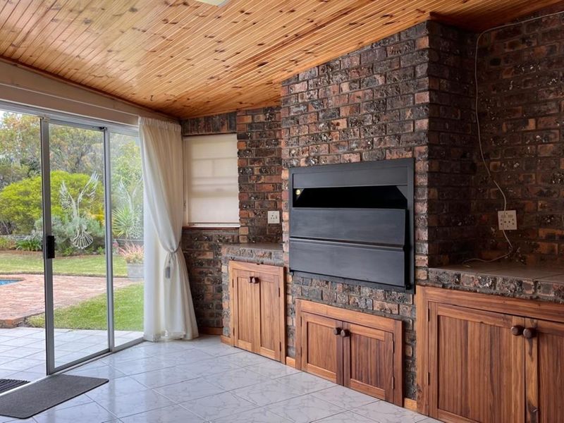 Covered patio featuring a built-in braai, exposed brickwork, timber ceiling, and sliding glass doors opening to the garden and pool area.