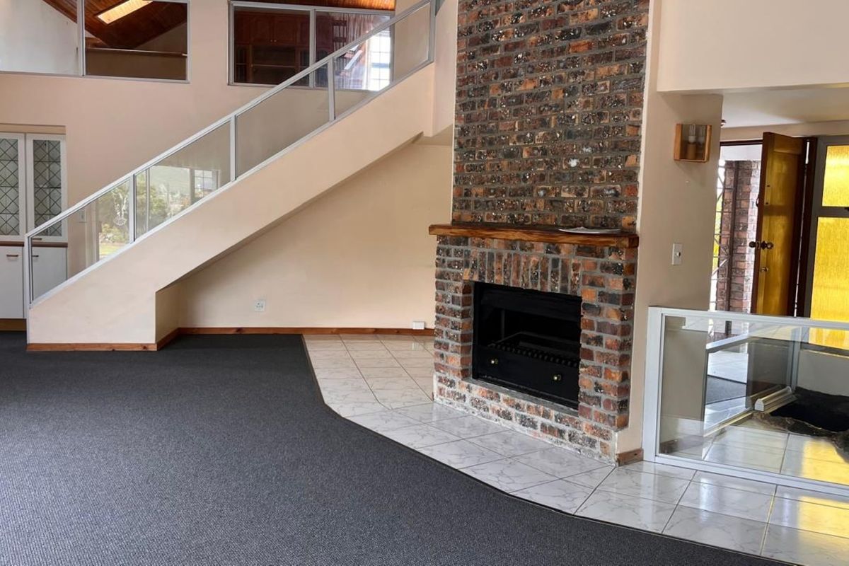 Spacious living area featuring a prominent brick fireplace, a modern staircase with glass balustrades, and a mix of carpet and tiled flooring.