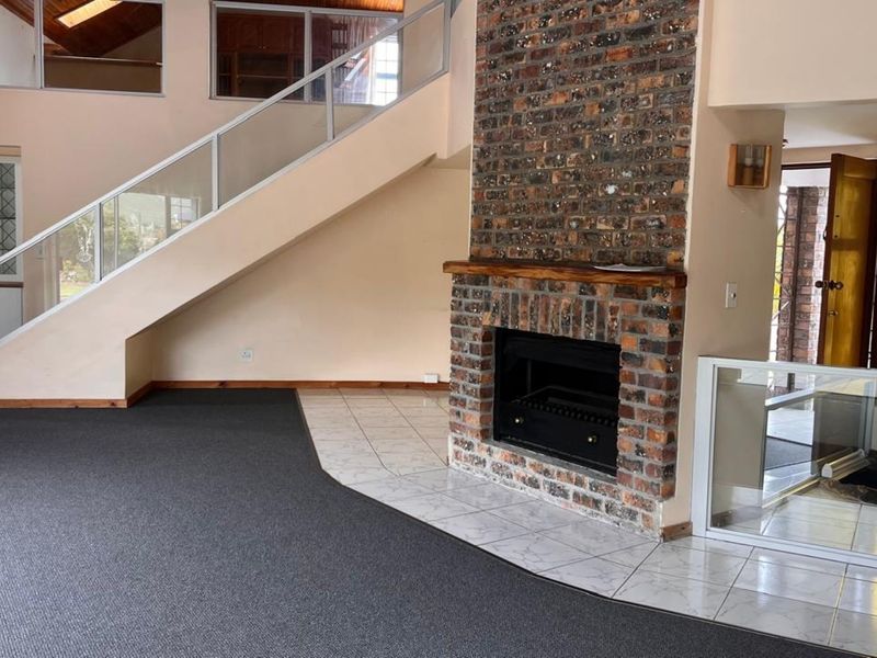 Spacious living area featuring a prominent brick fireplace, a modern staircase with glass balustrades, and a mix of carpet and tiled flooring.