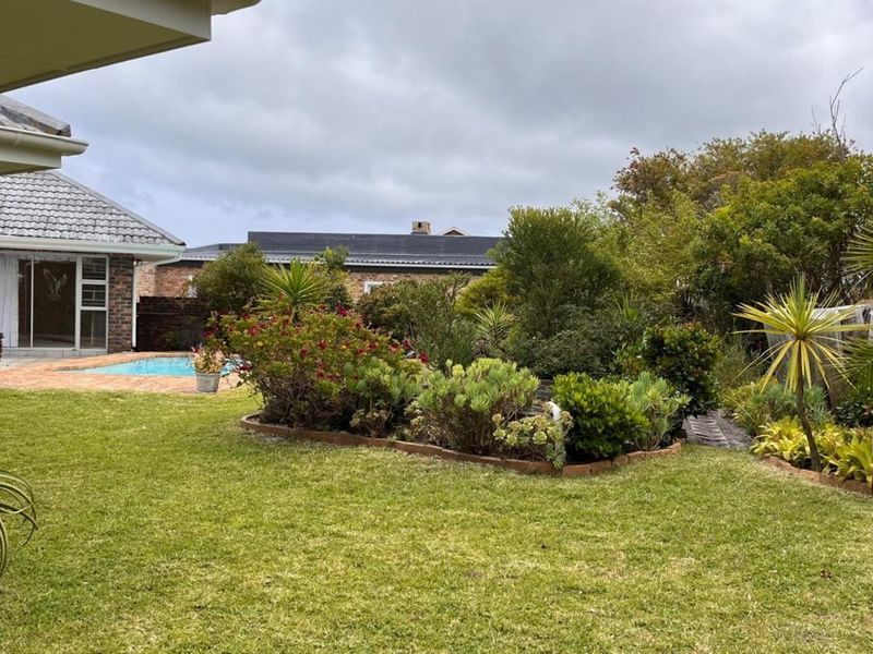 A well-maintained rear garden featuring a swimming pool with brick paving, established landscaping, and views of the property's rear elevation.
