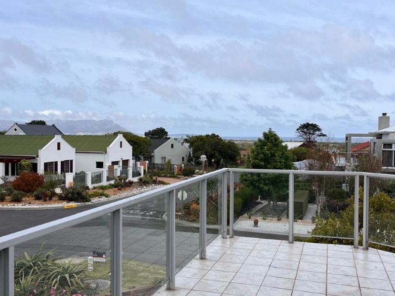 An elevated balcony featuring a modern glass balustrade and tiled flooring, offering expansive views of the surrounding neighbourhood and distant landscape.