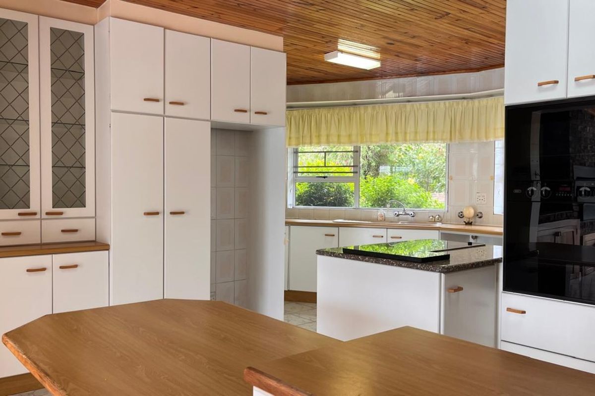 A spacious kitchen featuring white built-in cabinetry, a central island with a hob, built-in oven, and a distinctive timber-paneled ceiling.