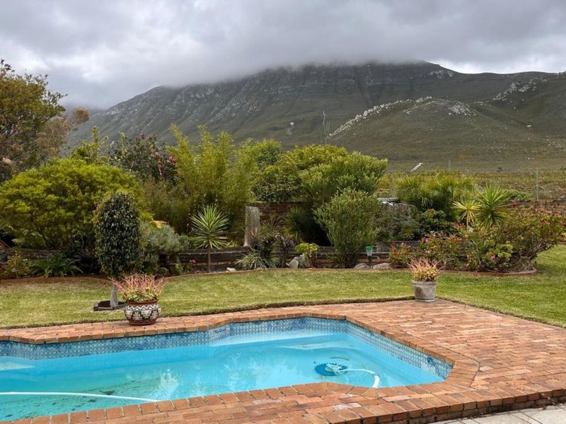 A well-maintained swimming pool area featuring brick coping, surrounded by a lush garden with scenic mountain views in the background.