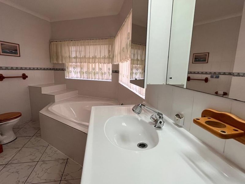 A functional bathroom featuring a built-in corner bathtub, vanity basin with mirror cabinet, and tiled finishes throughout.