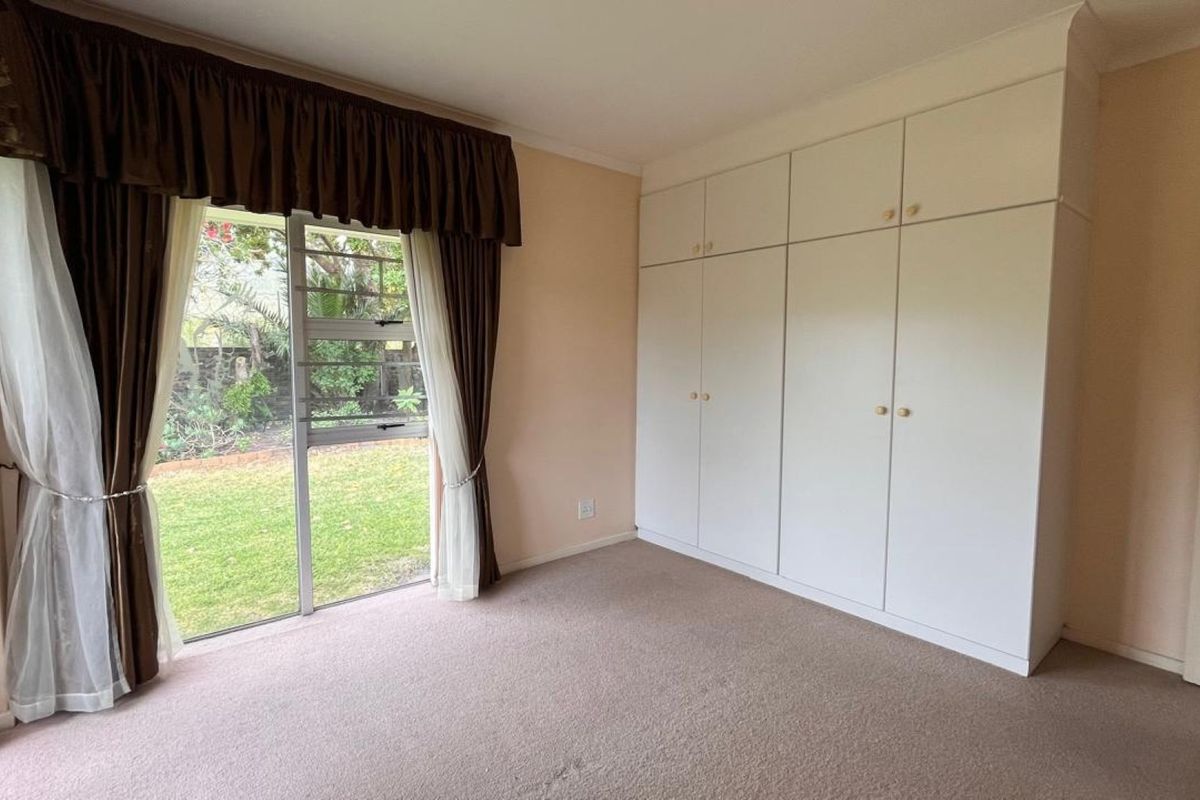 A spacious bedroom featuring built-in cupboards, carpeted flooring, and a sliding glass door providing direct access to the garden.