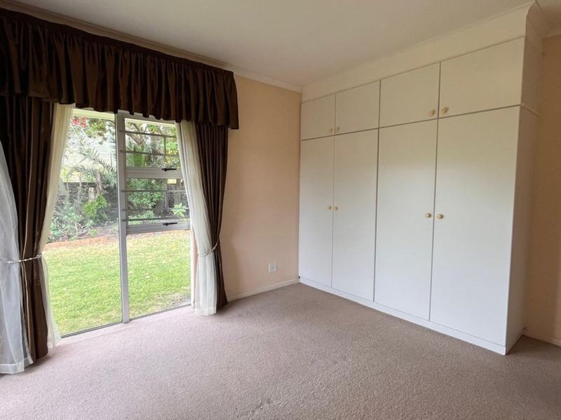 A spacious bedroom featuring built-in cupboards, carpeted flooring, and a sliding glass door providing direct access to the garden.