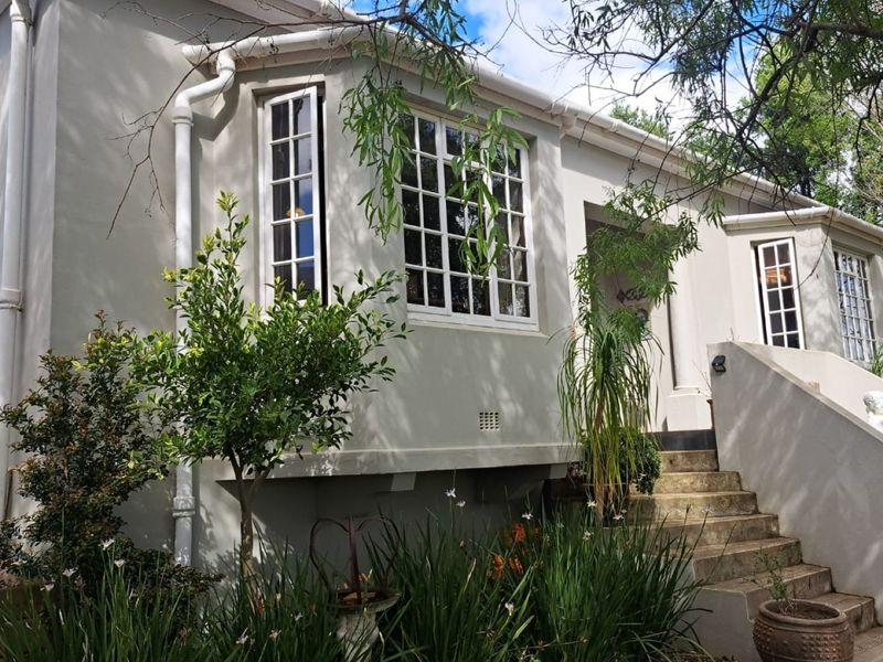 Front elevation of a charming house featuring classic bay windows, a concrete staircase entrance, and well-maintained plastered exterior walls.