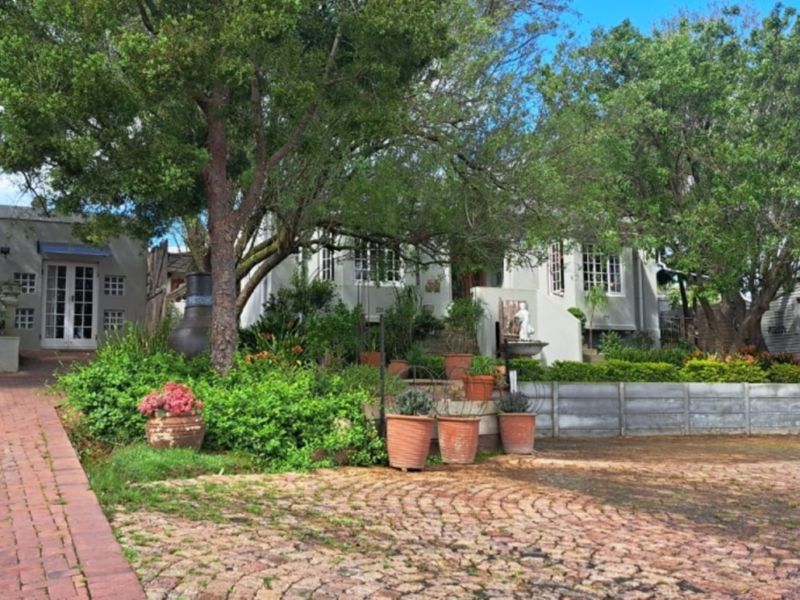 Front view of a charming house featuring a brick driveway, established trees, and a landscaped garden leading to the main entrance.