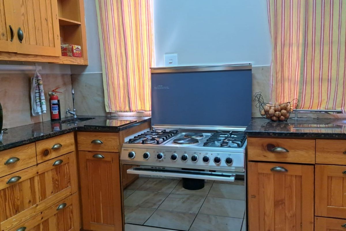 A functional kitchen featuring solid wood cabinetry, granite countertops, and a freestanding gas and electric stove combination with tiled flooring.