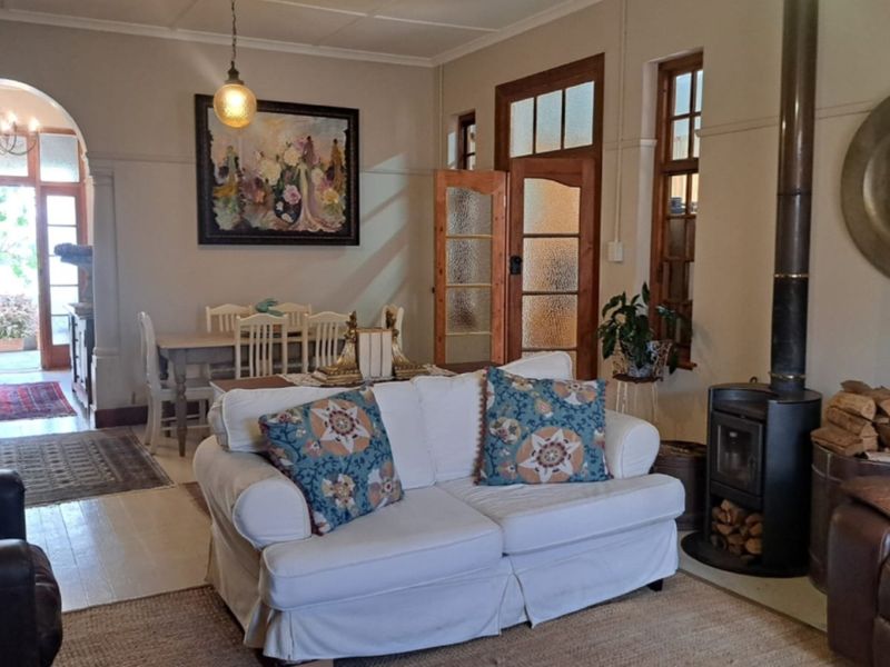 A cozy living room featuring a wood-burning stove, hardwood floors, and classic timber-framed glass doors leading to an adjacent dining area and exterior access.
