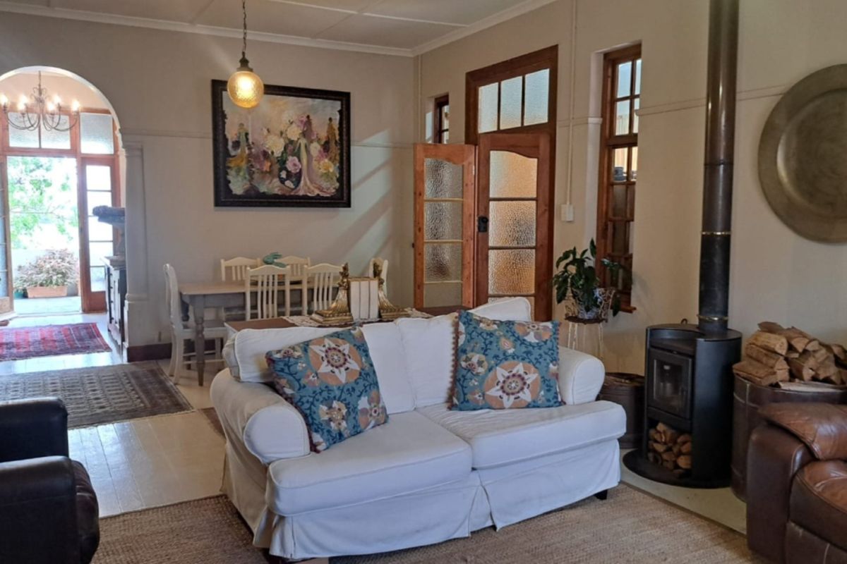 A cozy living room featuring a wood-burning stove, hardwood floors, and classic timber-framed glass doors leading to an adjacent dining area and exterior access.