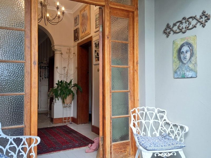 Inviting entrance featuring timber-framed glass doors, an elegant arched doorway, and a classic chandelier, leading into a warm and character-filled home interior.