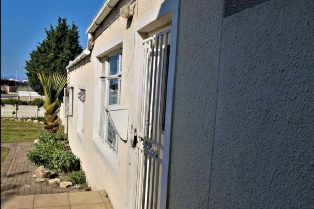 A side view of the property featuring a tiled patio area, security gate, and textured exterior walls with casement windows.