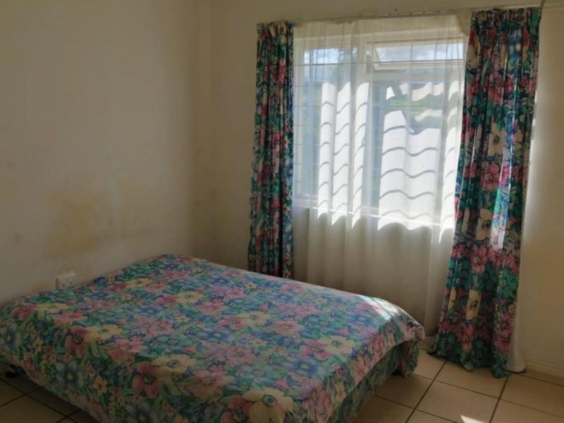 A bedroom featuring tiled flooring and a window, currently showing signs of wall staining and dated finishes.