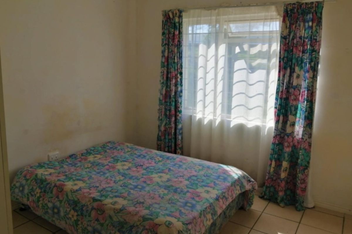 A bedroom featuring tiled flooring and a window, currently showing signs of wall staining and dated finishes.